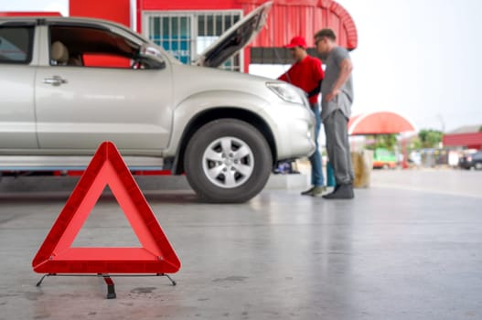 Red triangle reflector roadside warning on the floor. There is a broken pickup car in the background.