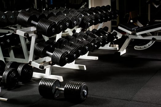 many black dumbbells in dark weight room, horizontal photo