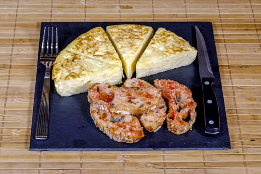 A triangle of potato Spanish omelette prepared on slate plate and covered with bread with tomato
