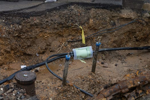 Dug up sidewalk revealing wires in protective tubes. Building of electric lines or telecommunication cables, construction of optical network connection. Excavation and maintenance