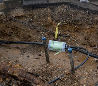 Dug up sidewalk revealing wires in protective tubes. Building of electric lines or telecommunication cables, construction of optical network connection. Excavation and maintenance