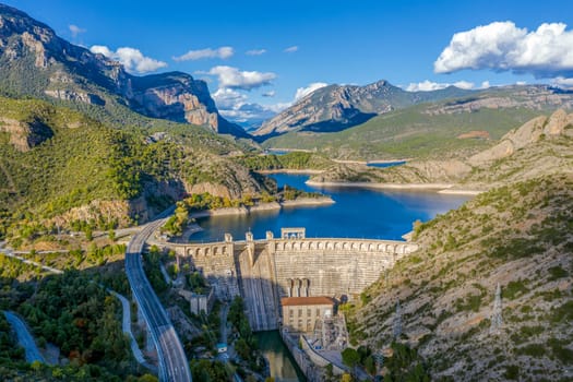 View of hydro-electric power station and a highway. Dam at Segre river, Oliana, Spain, Europe. Mountain peaks landscape
