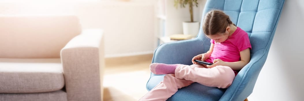 Cute girl sitting on the sofa and playing in the smartphone. Concept of leisure activity of the new generation.