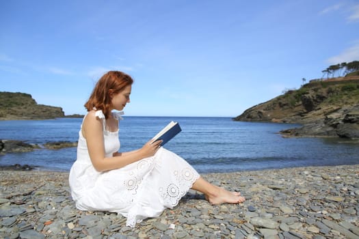 Woman in white dress reading a book on the beach