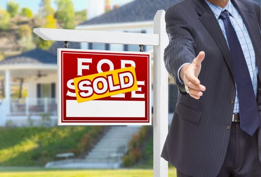 Male Agent Reaching for Hand Shake in Front of Sold For Sale Sign and House.