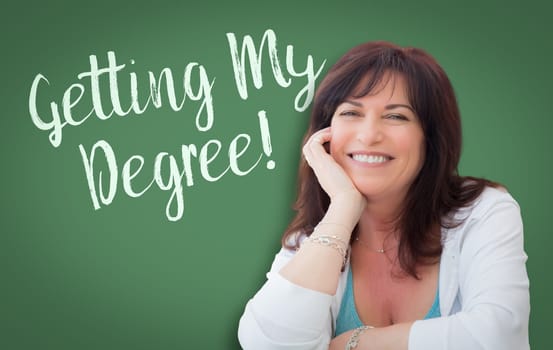 Getting My Degree Written On Green Chalkboard Behind Smiling Middle Aged Woman.