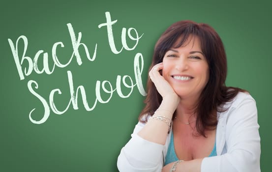 Back To School Written On Green Chalkboard Behind Smiling Middle Aged Woman.