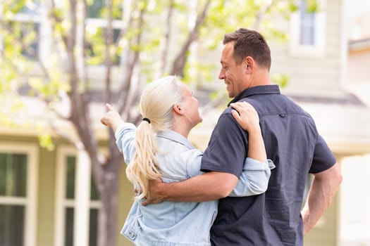 Happy Caucasian Couple Facing and Pointing to Front of House.