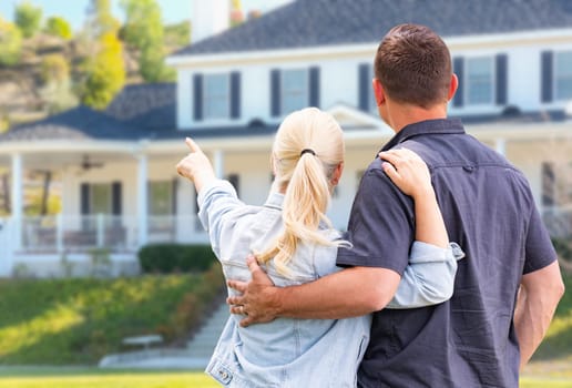 Young Adult Couple Facing and Pointing to Front of House.