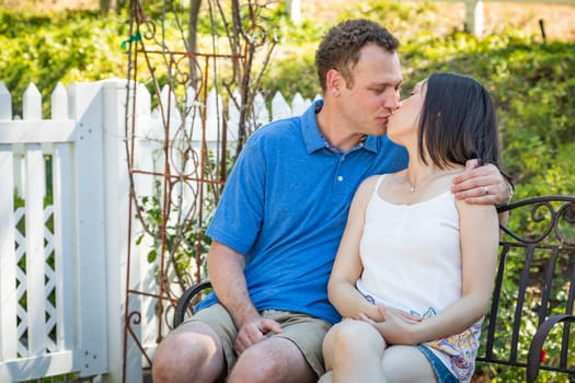 Young Caucasian Man and Chinese Woman Sitting On Bench Kissing