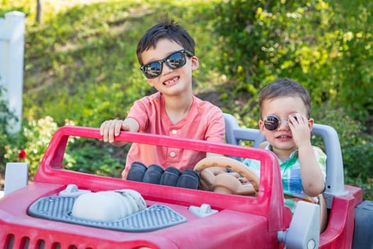 Young Mixed Race Chinese and Caucasian Brothers Wearing Sunglasses Playing In Toy Car