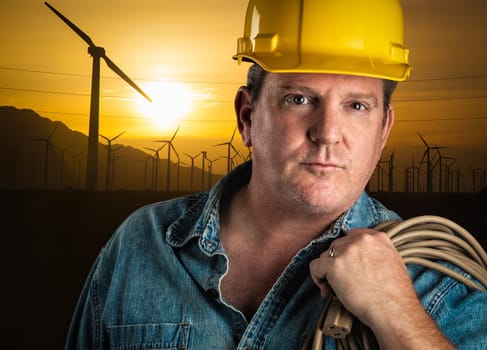 Serious Contractor in Hard Hat Holding Extension Cord Outdoors Near Wind Turbines.