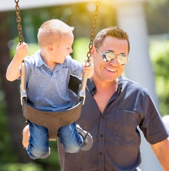 Happy Young Boy Having Fun On The Swings With His Father At The Playground.