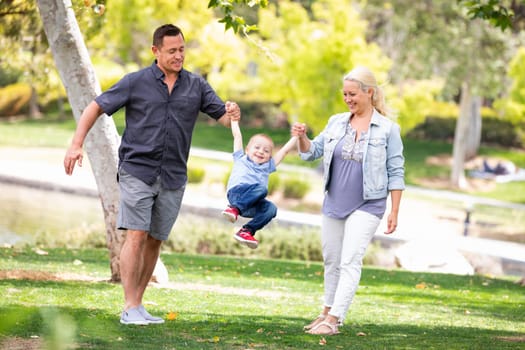 Young Mother and Father Swingging Their Son At The Park.