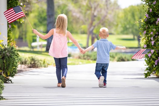 Young Sister and Brother Holding Hands and Waving American Flags At The Park.