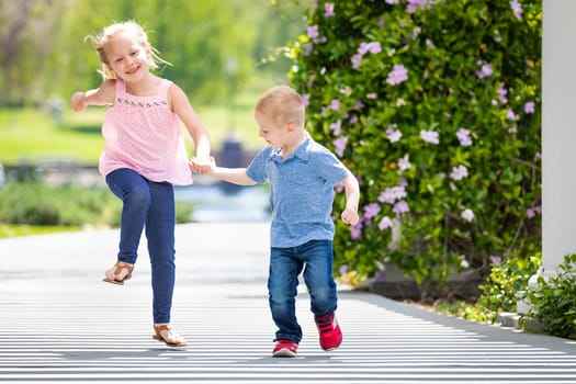 Young Sister and Brother Holding Hands And Running At The Park.