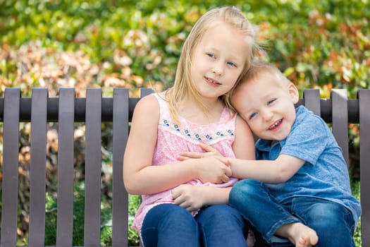 Young Sister and Brother Having Fun On The Bench At The Park.