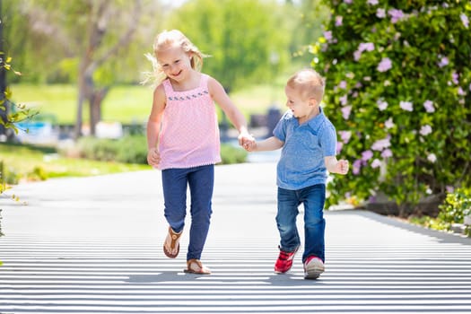 Young Sister and Brother Holding Hands And Running At The Park.