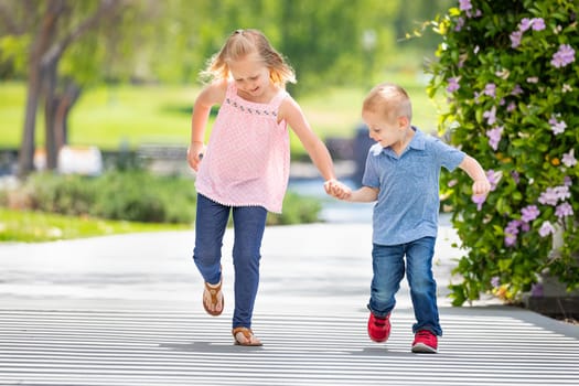 Young Sister and Brother Holding Hands And Running At The Park.