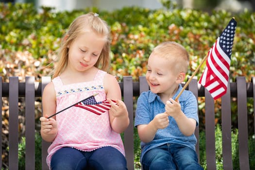 Young Sister and Brother Comparing Each Others American Flag Size On The Bench At The Park.