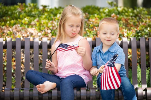 Young Sister and Brother Comparing Each Others American Flag Size On The Bench At The Park.