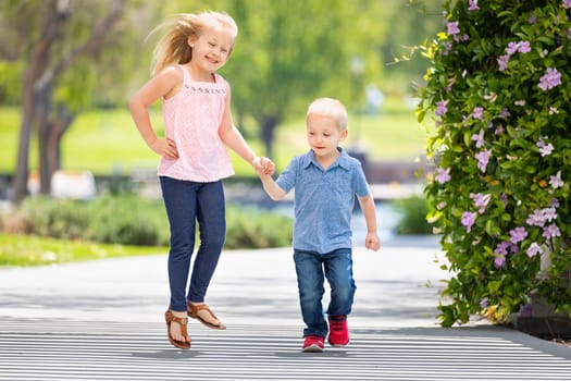 Young Sister and Brother Holding Hands And Running At The Park.