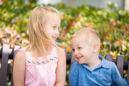 Young Sister and Brother Having Fun On The Bench At The Park.