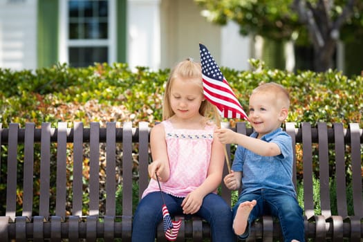 Young Sister and Brother Comparing Each Others American Flag Size On The Bench At The Park.