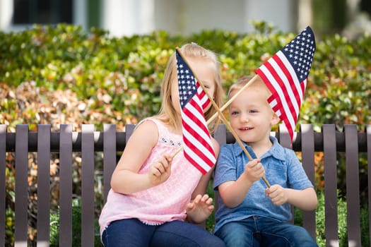 Young Sister and Brother Waving American Flags On The Bench At The Park.