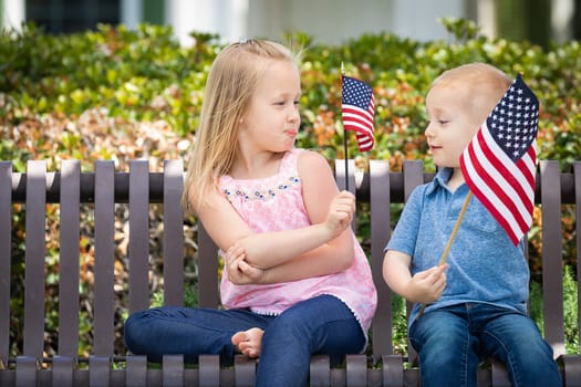 Young Sister and Brother Comparing Each Others American Flag Size On The Bench At The Park.
