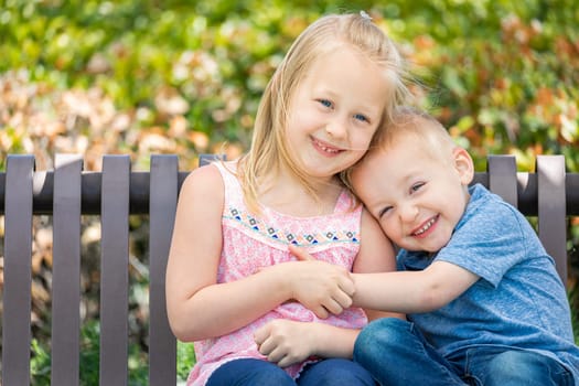 Young Sister and Brother Having Fun On The Bench At The Park.