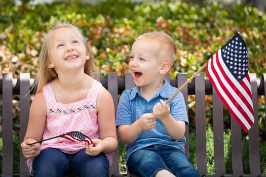 Young Sister and Brother Comparing Each Others American Flag Size On The Bench At The Park.