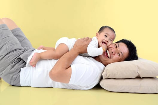 Happy father's day! joyful young dad  hugging his cute son and lying on floor at home. Isolated on yellow background..