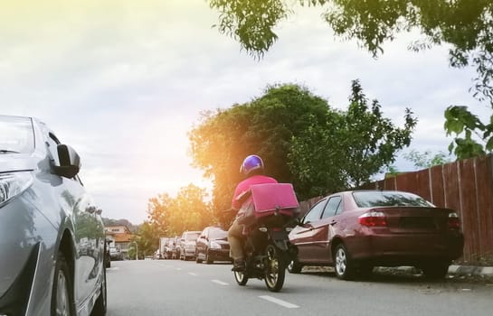 Motorbike delivery man with isothermal food pink case box  delivering food in an asian city.Express food delivery service.