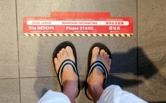 Lines pasted on floors in chinese, malay and english language to provide people a safe distance from each other in supermarket during the Coronavirus pandemic at Kuala Lumpur, Malaysia.
