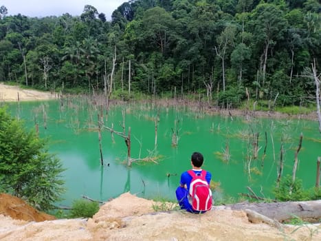 Asian man relaxing with serene view mountains and green lake landscape Vacations and travel lifestyle hiking concept.
