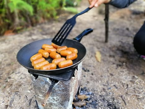 Fire delicious sausages cooking in a pan over campfire.Summer picnic.