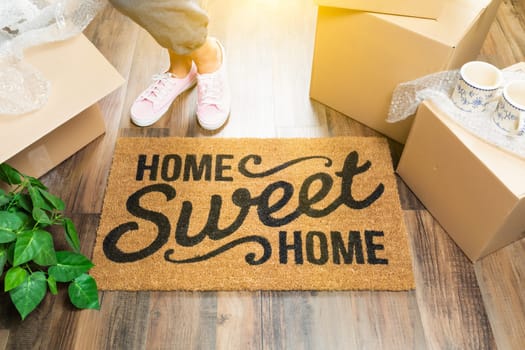Woman in Pink Shoes and Sweats Standing Near Home Sweet Home Welcome Mat, Boxes and Plant.
