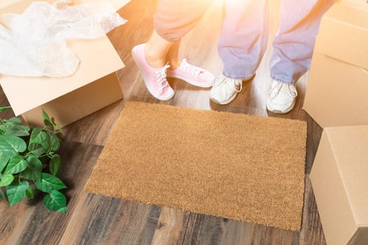 Man and Woman Standing Near Home Sweet Home Welcome Mat, Moving Boxes and Plant.