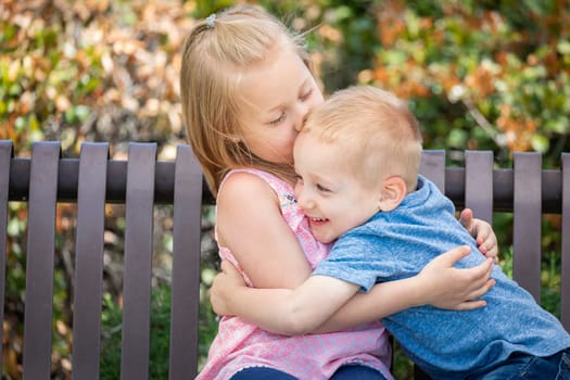 Young Sister and Brother Having Fun On The Bench At The Park.