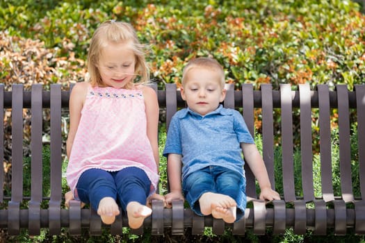 Young Sister and Brother Having Fun On The Bench At The Park.