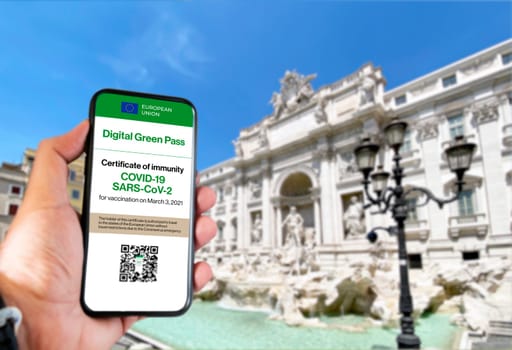 Hand holding a phone with The digital green pass of the european union with the QR code on the screen with blurred Trevi fountain in the background. Immunity from Covid-19. Travel destination