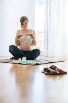 Happy Caucasian pregnant mother is sitting on the floor, reading about pregnancy, blue jeans