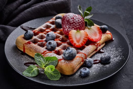 Delicious waffles with  powdered sugar and berries on ceramic black plate on grey background. Sweet meal. Dessert. Serving food