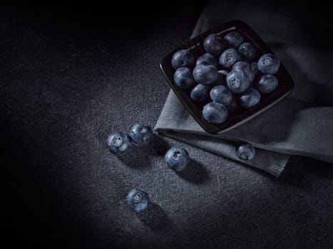 Ripe blueberries (bog whortleberry, great bilberry) in black bowl on dark grey background. Top view