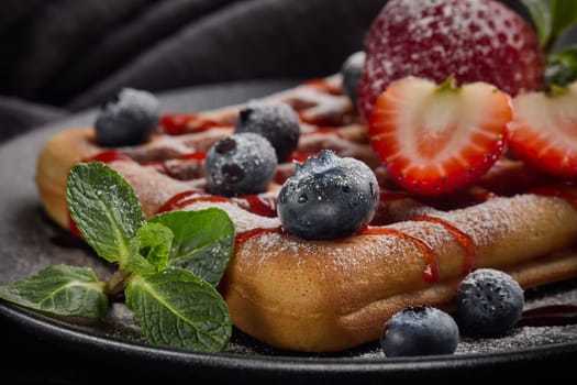 Delicious waffles with  powdered sugar and berries on ceramic black plate on grey background. Sweet meal. Dessert. Serving food