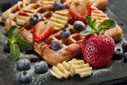 Delicious waffles with berries, mint, powdered sugar and sweet sauce  on slate serving board on grey background. Sweet meal. Dessert. Serving food