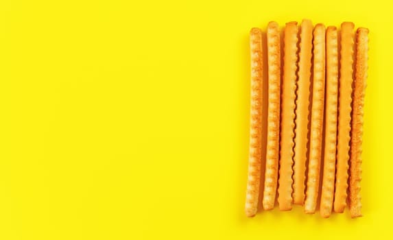 Grissini, also known as breadsticks on yellow board, view from above space for text left side.
