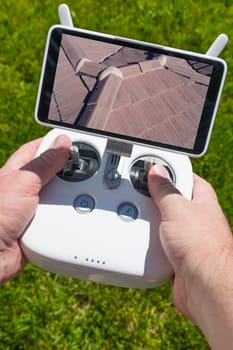 Hands Holding Drone Quadcopter Controller With Residential Roof Image on Screen.