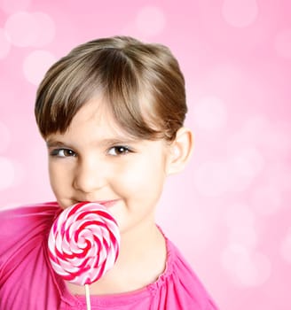 Beautiful little girl with lolipop in front of the pink background